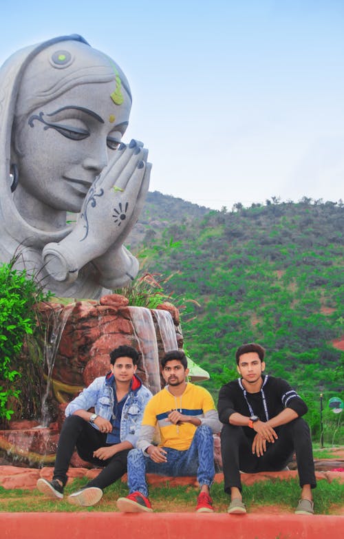 Three Friends Sitting Infront Of Old Statue Surrounded  With Mountains