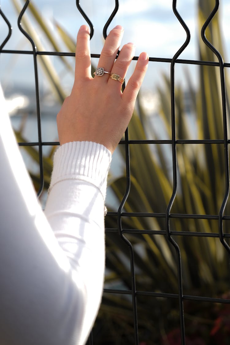 Person Wearing Gold Rings Holding On Fence