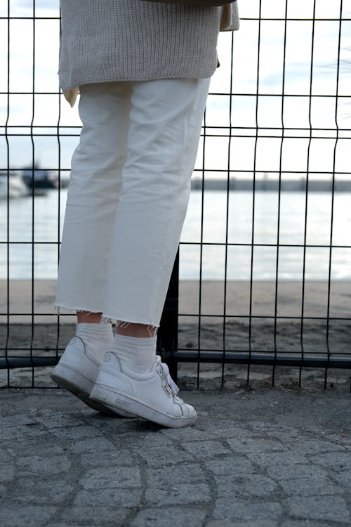 A Person in White Pants and White Sneakers Tip Toeing on Gray Concrete Floor Near Wire Fence