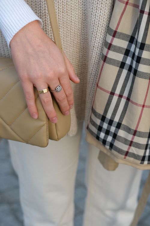 Free Elegant close-up of a woman's hand, showcasing rings, a beige quilted purse, and a stylish plaid scarf. Stock Photo