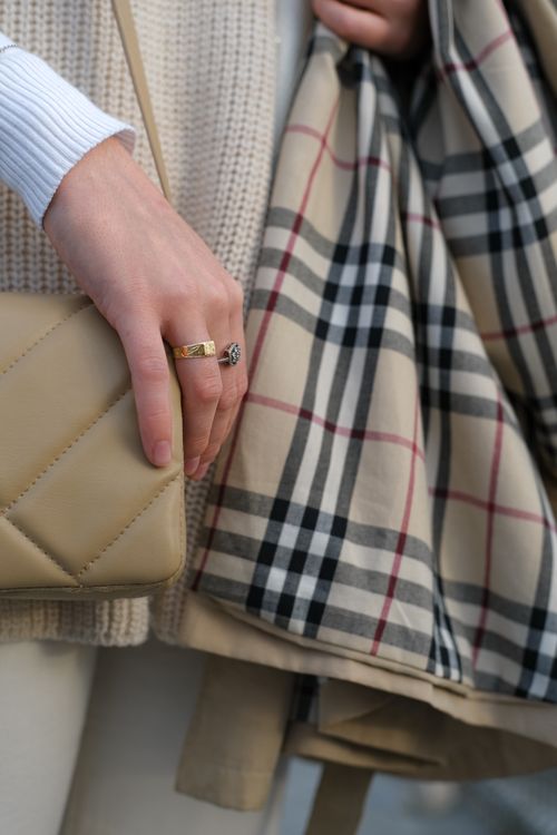 Free Close-up of an elegant hand with a gold ring, holding a checkered scarf and beige bag. Stock Photo