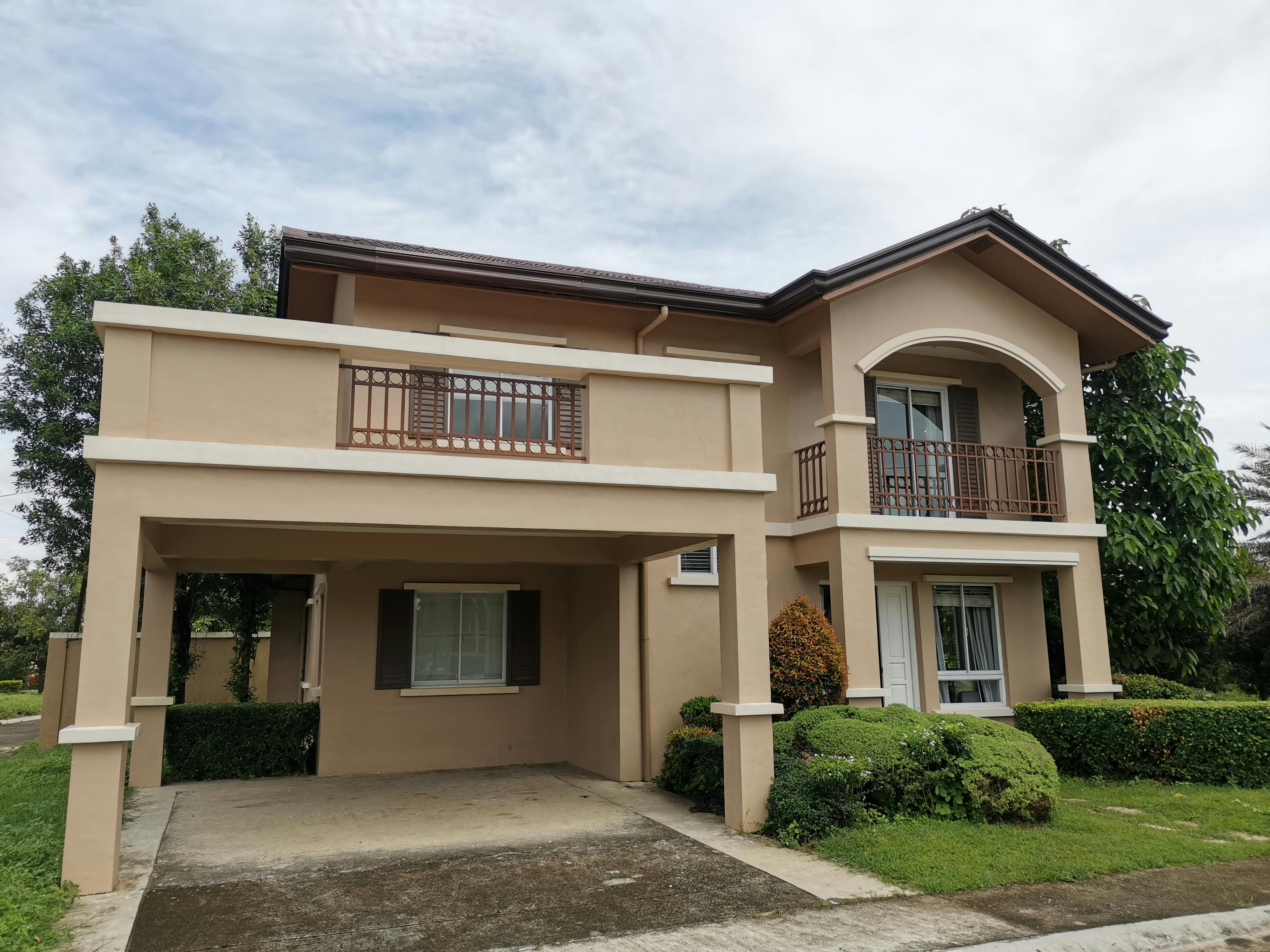 A modern two-storey house with a balcony, garage, and manicured garden in a suburban area.