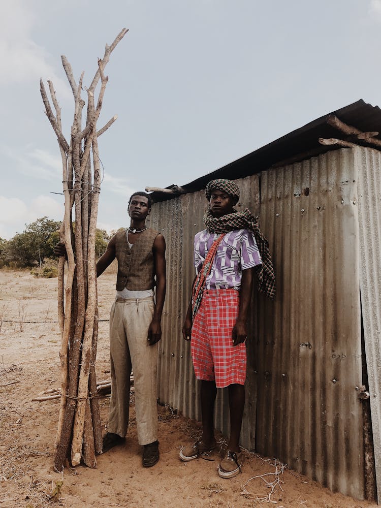 Two African Man Standing Next To To A Tin Hut 