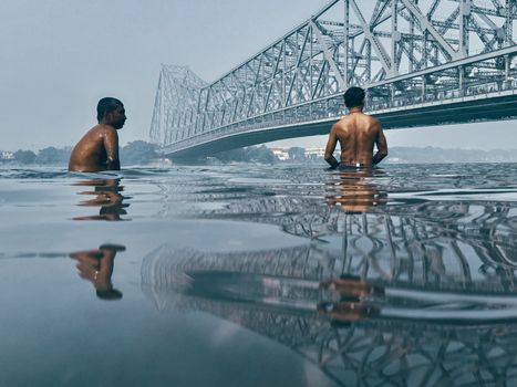 Men enjoy a swim in the Hooghly River with Howrah Bridge in the backdrop, Kolkata.