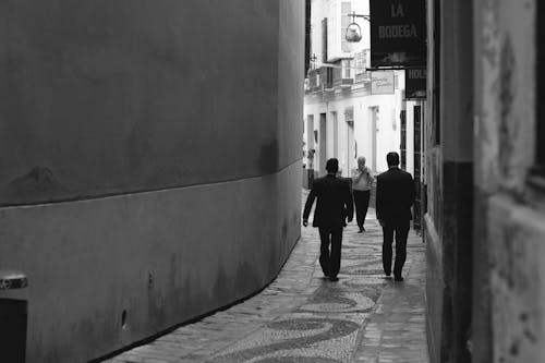 Grayscale Photo of Men Walking Near Wall