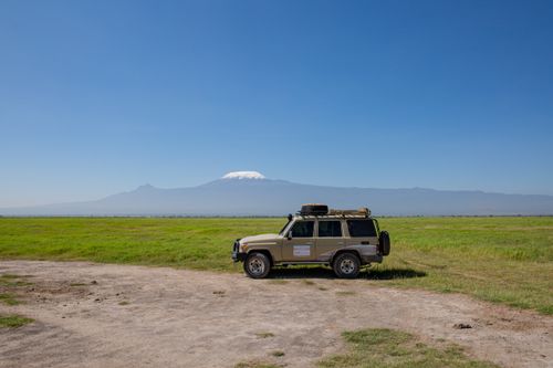 Free A 4x4 vehicle parked on a savannah with Mount Kilimanjaro in the background, highlighting adventure and exploration. Stock Photo