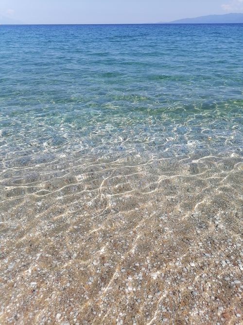 Free Clear sea waves gently lap over a sandy beach with a scenic horizon view. Stock Photo