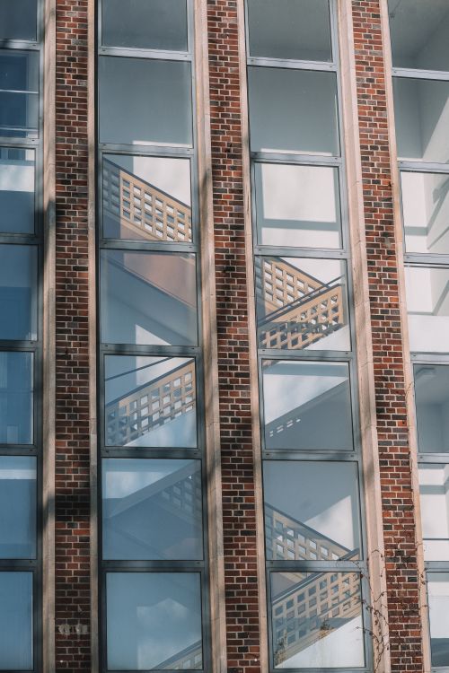 Free Vertical view of a modern building facade with glass windows and brick design, featuring a staircase behind the glass. Stock Photo