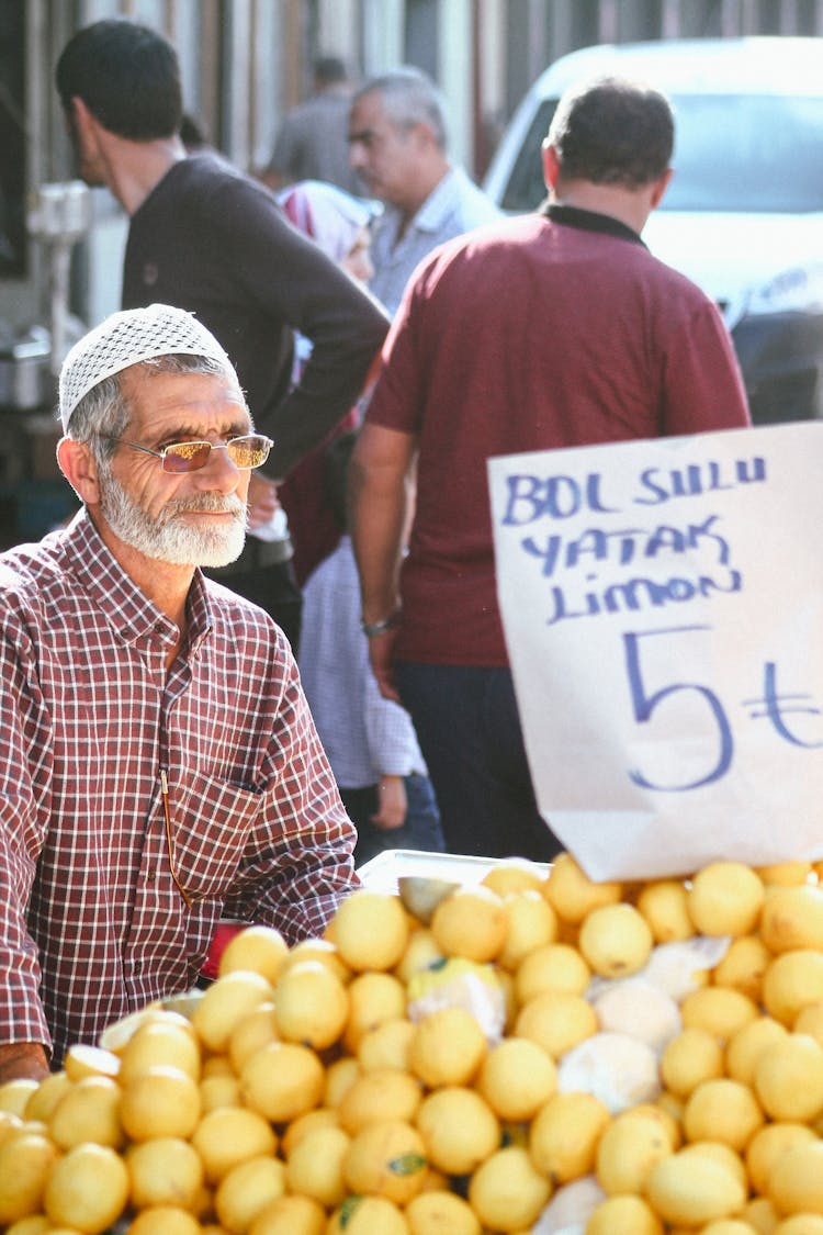 Senior Man In Red And White Plaid Button Up Shirt Selling Orange Fruits On Marketplace