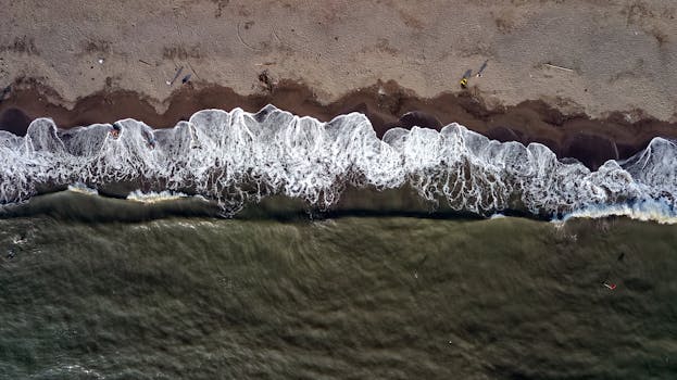 Drone aerial view of Teluknaga beach in Banten, Indonesia showcasing waves crashing on sandy shore.