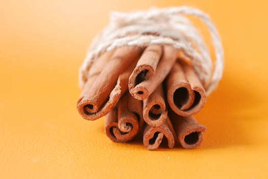 Close-up of a bundle of cinnamon sticks tied with rope against an orange background.