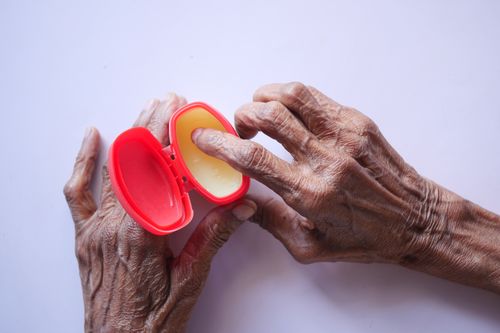Free Close-up of senior hands using hand cream for skincare in a red container on a white background. Stock Photo
