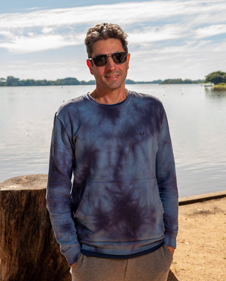 Man In Blue Tie Dye Sweater Standing Beside Body Of Water