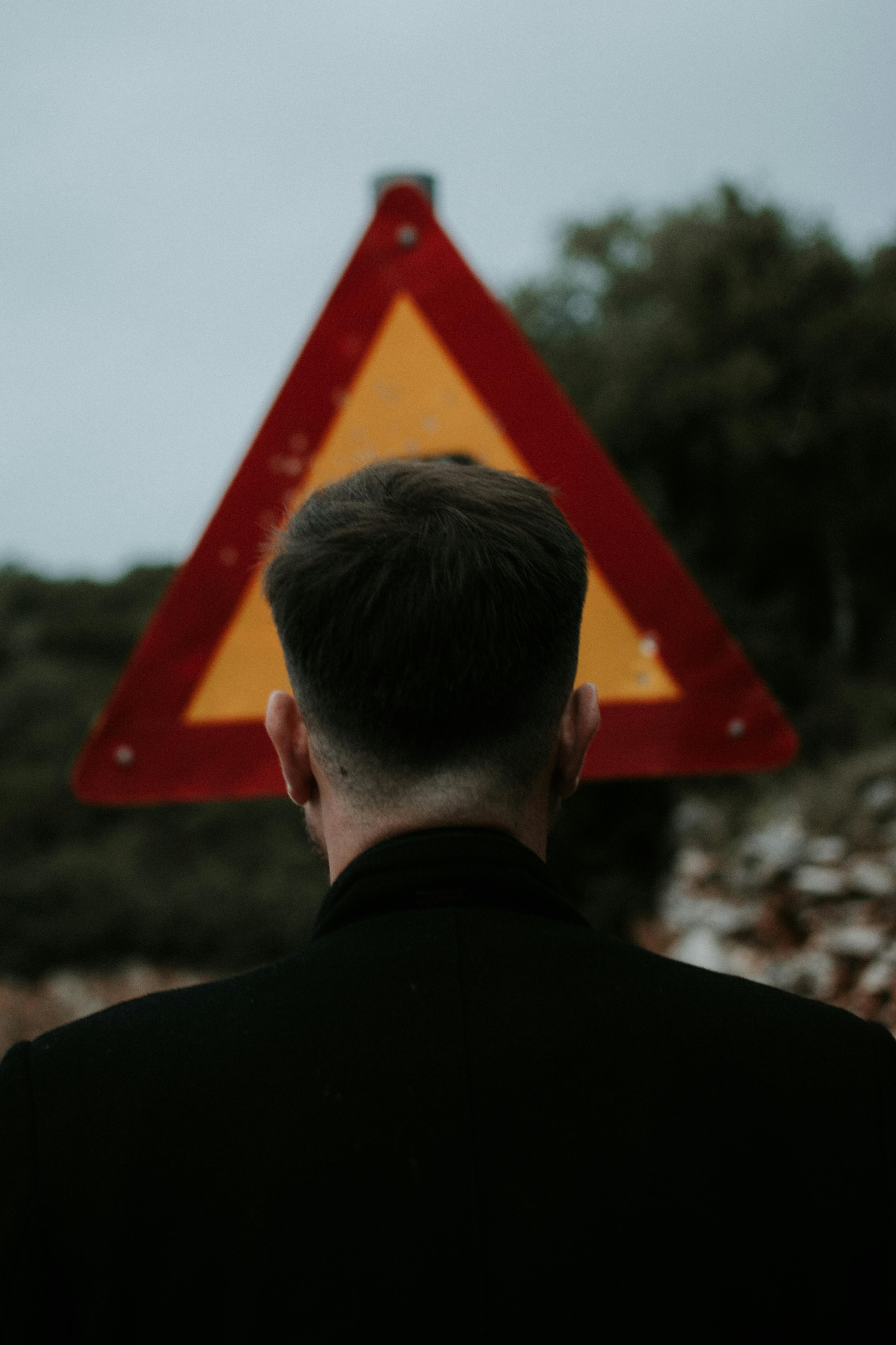 Back view of a man standing by a caution sign on an outdoor road.
