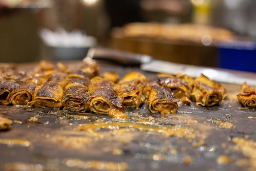 Close-up of crispy rolled pancakes freshly fried on a griddle, showcasing indulgent dessert preparation.