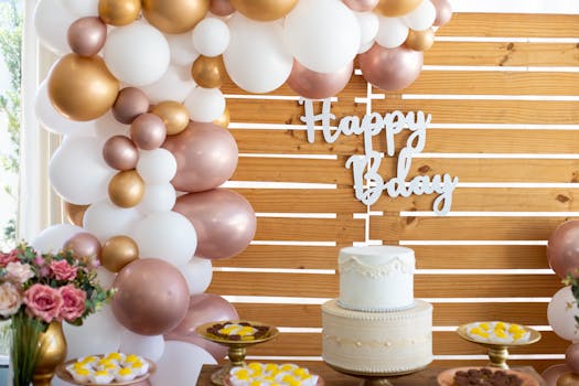 A beautifully decorated birthday setup with a white cake, balloons, and floral arrangements indoors.