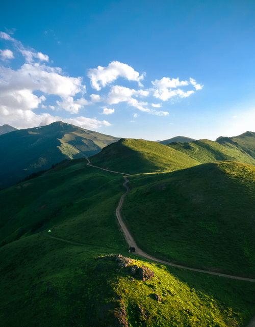 Free A breathtaking view of lush green mountains with a winding dirt road under blue skies. Stock Photo
