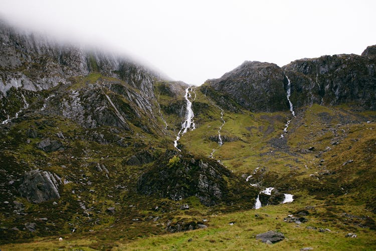 A Green Grass Field And Mountain Under The White Sky