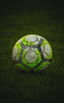Close-up of a worn soccer ball resting on a green field in Adana, Turkey.
