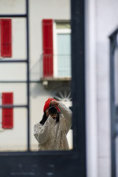 Photographer capturing their reflection against urban architecture with red shutters.