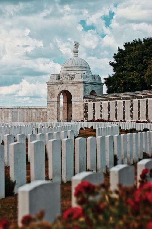 Free Peaceful view of Zonnebeke cemetery with rows of tombstones and a memorial against a cloudy sky. Stock Photo