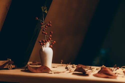 A White Ceramic Vase With Red Berries on a Brown Surface