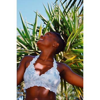 一位穿着蕾丝文胸、面带微笑的女子，正在享受大自然，周围是明亮的绿叶和清澈的蓝天