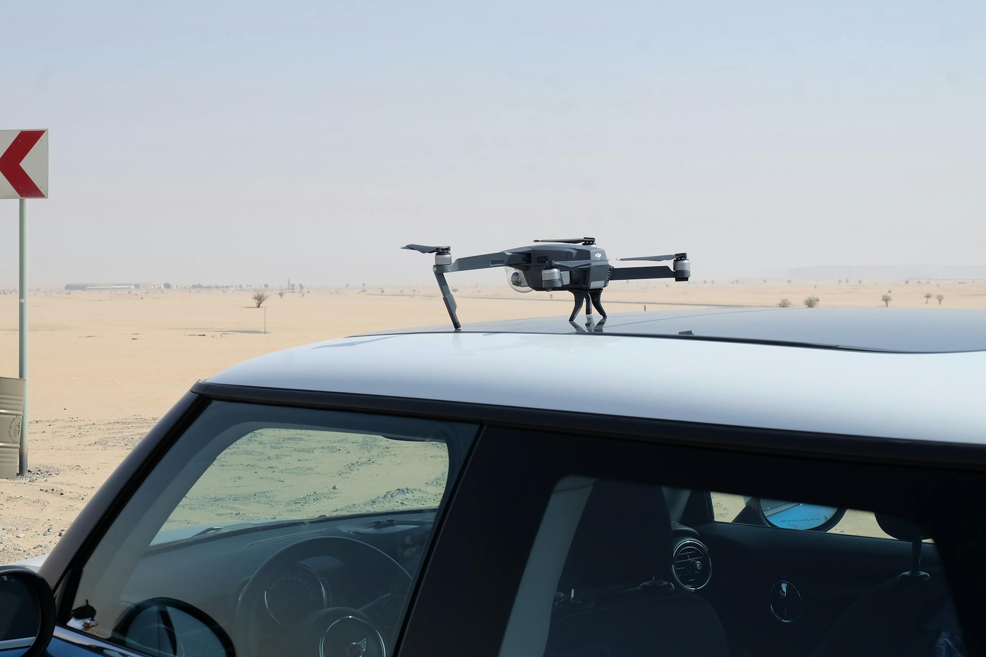 A drone rests on a car roof in the Dubai desert with clear skies.