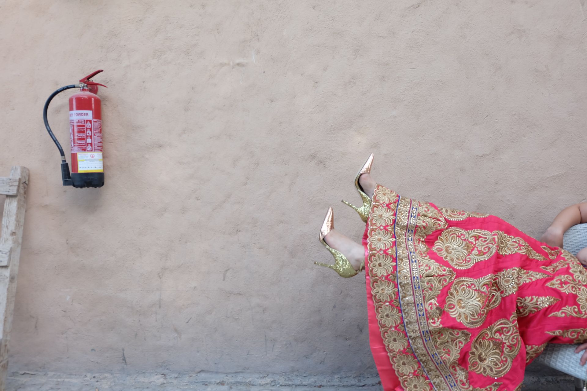 A striking composition featuring golden stilettos and a decorative skirt against a wall-mounted fire extinguisher.