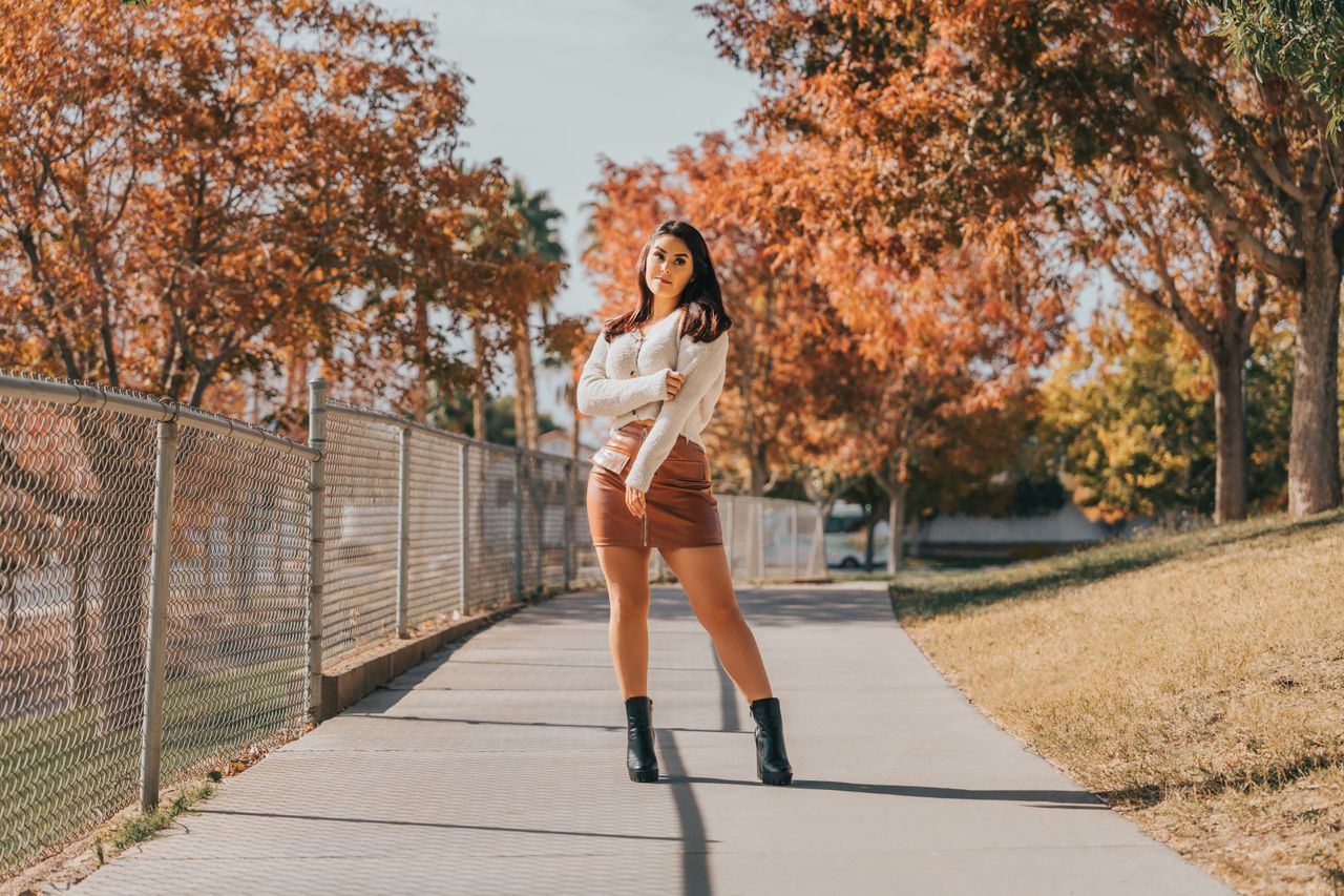 Woman in a white cardigan and brown suede-look mini skirt with black ankle boots on an autumn path