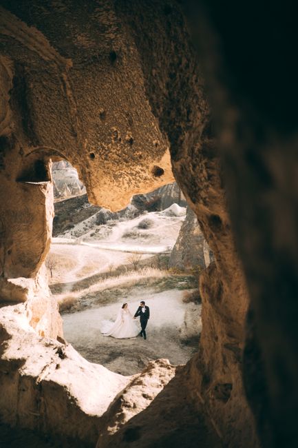 A wedding couple walking through a scenic rocky terrain captured through a cave view.