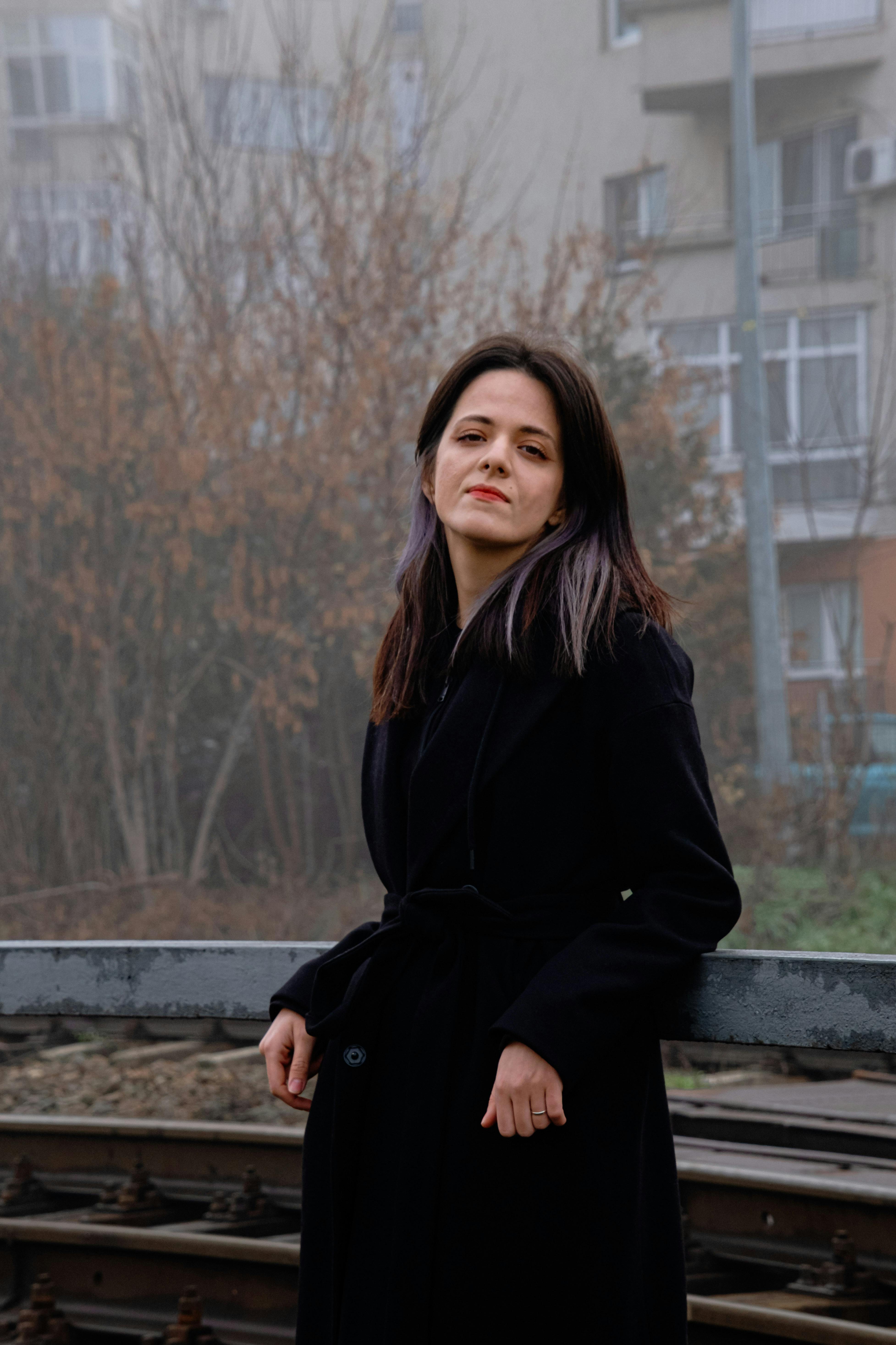 Portrait of a woman in a black coat by urban train tracks on a foggy day.