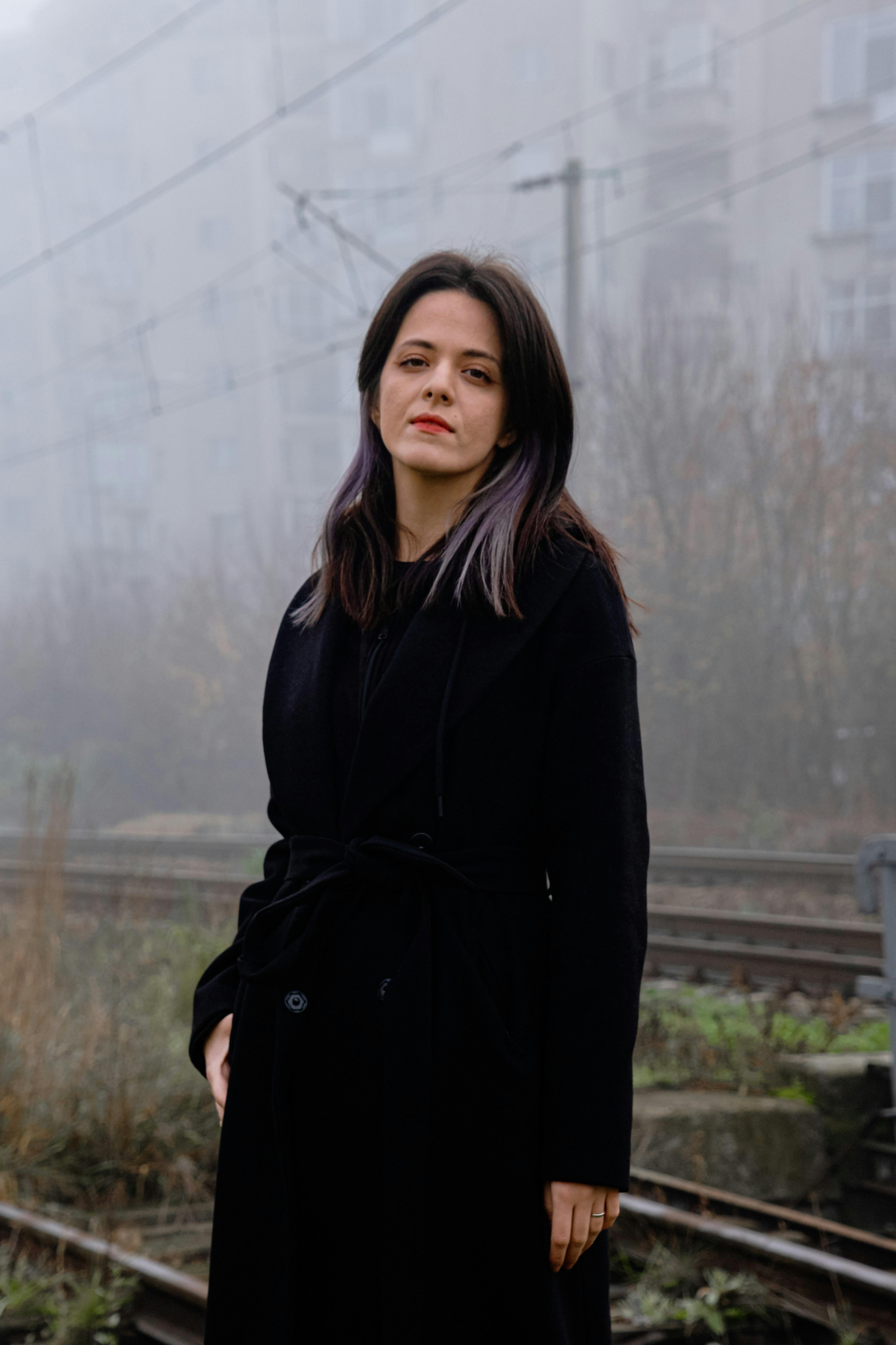 Portrait of a woman in a black coat on a foggy day near train tracks.