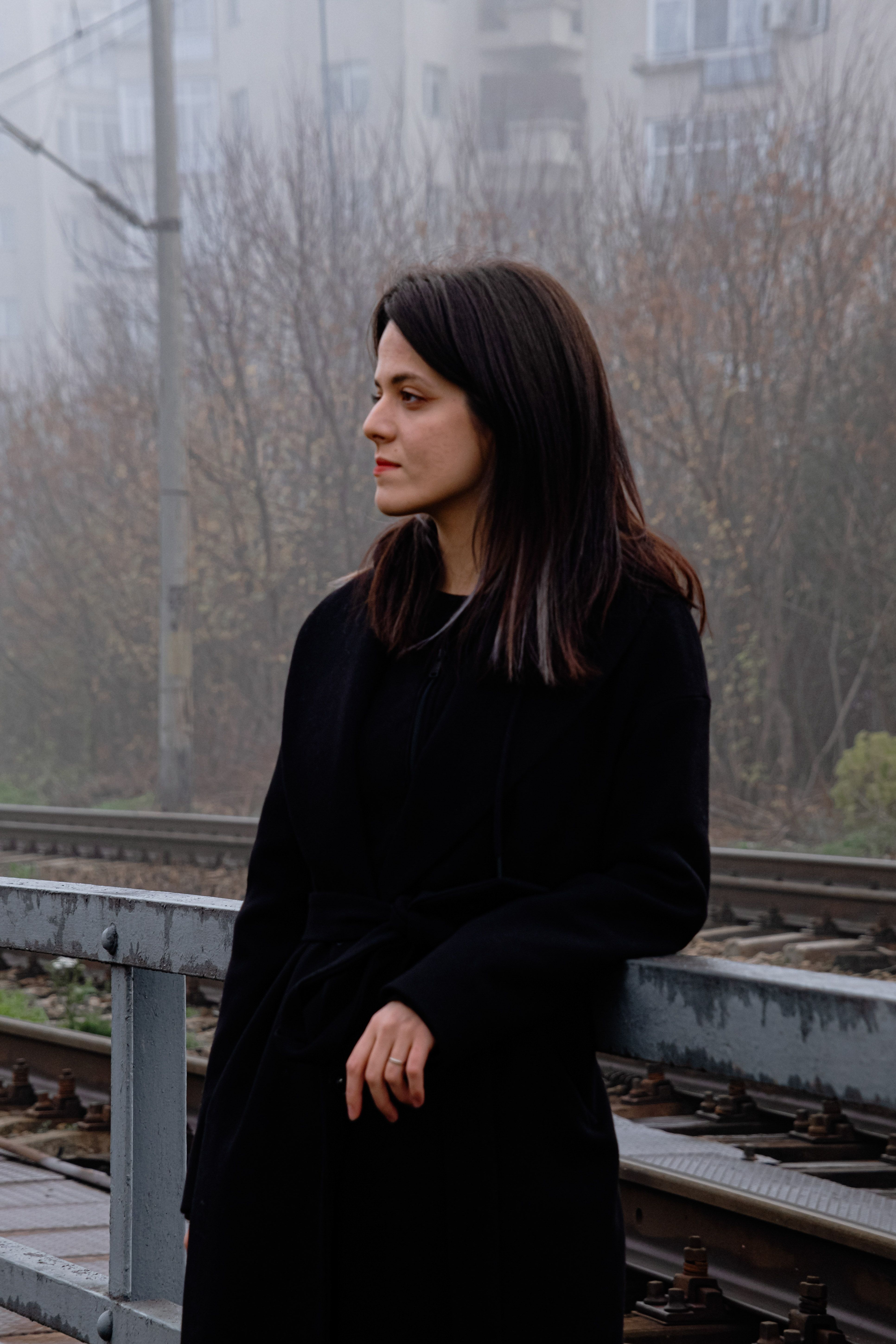 Caucasian woman standing by foggy railway in autumn, wearing a black coat.