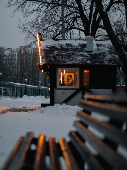 Free A cozy cabin illuminated in winter snow with a visible bench in the foreground. Stock Photo