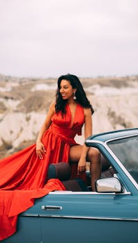 Stylish woman in a red dress posing in a convertible car outdoors.