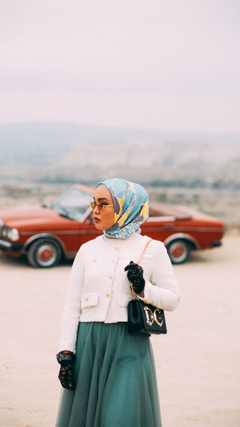 Perempuan berhijab di samping mobil klasik