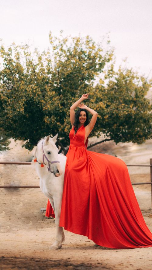 Free A smiling woman in a vibrant red dress on horseback, set against a natural background. Stock Photo