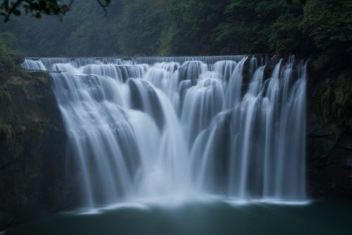 Free Breathtaking long exposure shot of a cascading waterfall surrounded by dense forest. Stock Photo