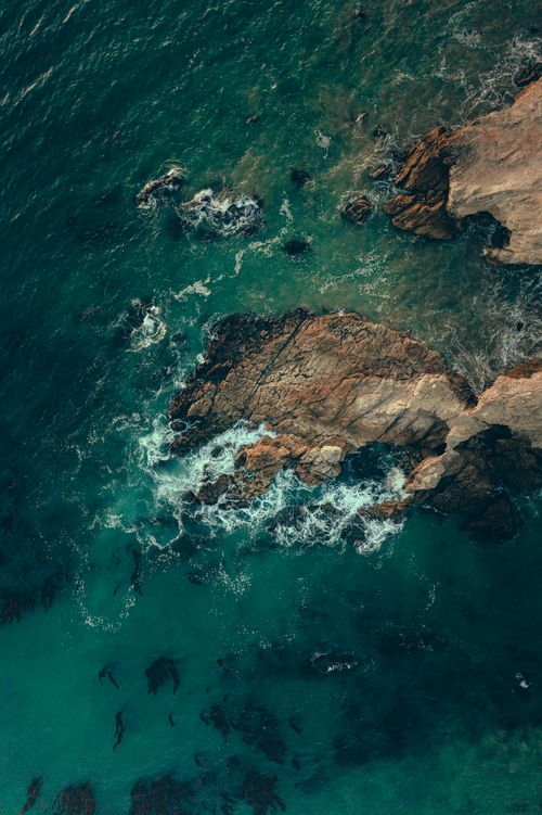 Free Stunning aerial shot capturing the rugged rocky shoreline meeting the turquoise ocean waves. Stock Photo