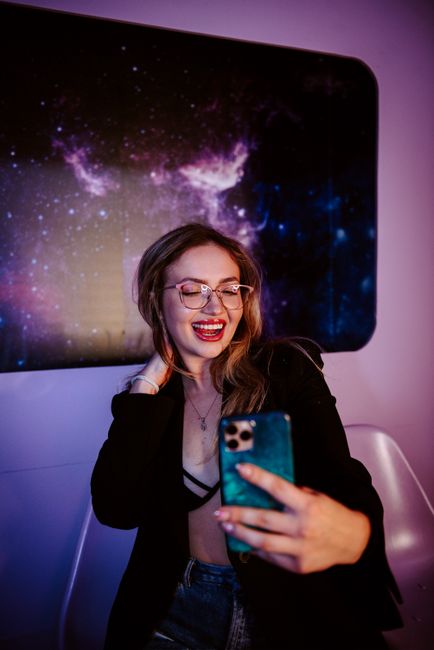 Happy woman taking a selfie against a vibrant galaxy-themed backdrop, showcasing modern lifestyle.