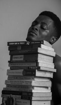 Black-and-white portrait of man balancing a tall stack of books. Educational and focused.