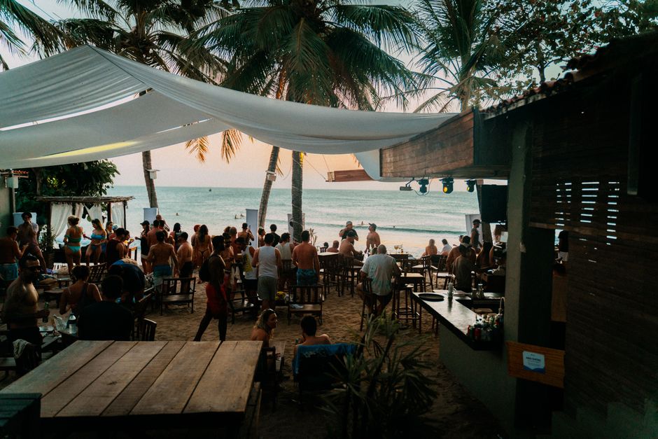 A vibrant beachside bar scene with people enjoying the sunset under palm trees. - The Boatyard Barbados: Daytime Beach Club to Nighttime Party