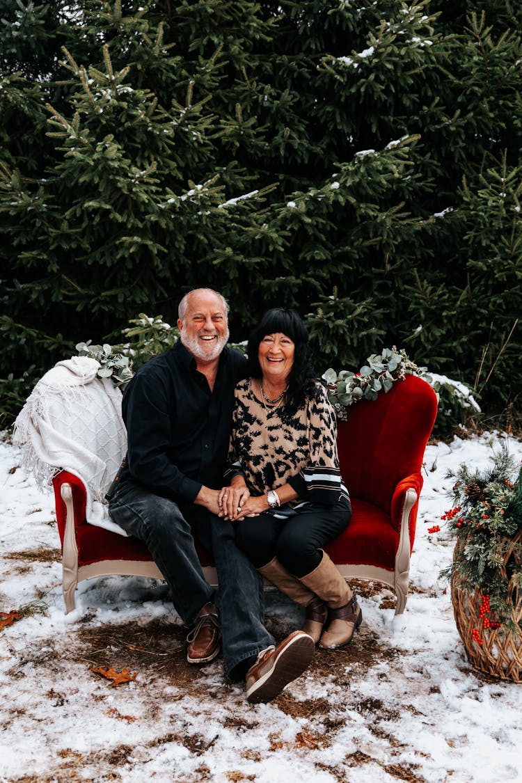 A Happy Elderly Couple Sitting On Red Sofa Outside