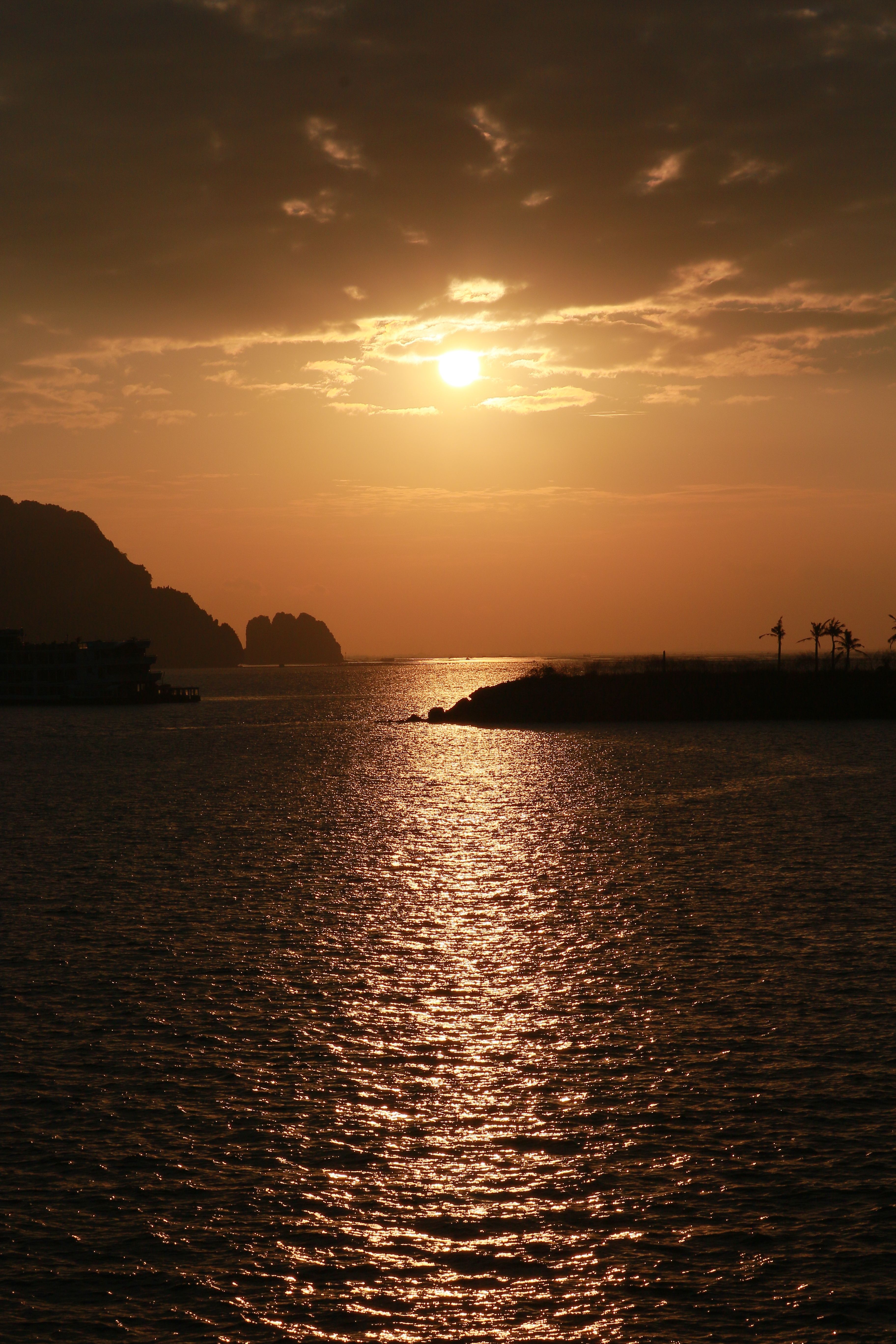 Serene sunset over Hạ Long Bay with a golden sky and rippling water in Vietnam.