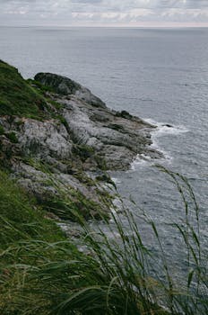 Scenic view of a rocky coastline with waves crashing against the shore under a cloudy sky.