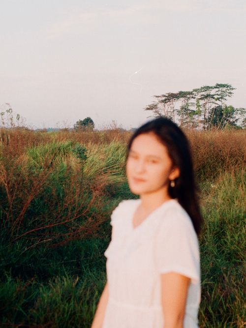 Free Blurred portrait of woman in white dress amidst lush green field with evening light. Stock Photo