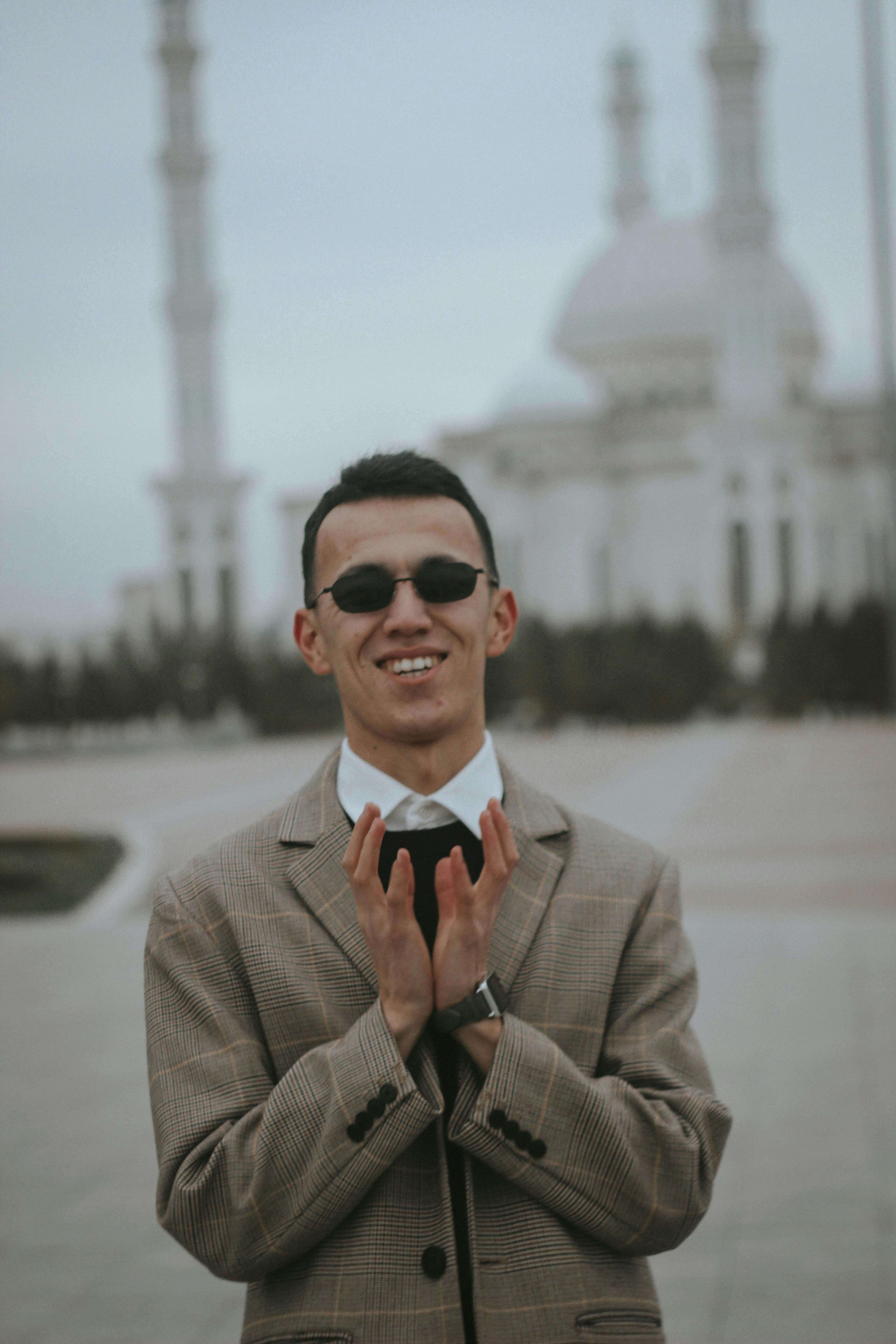 A man in sunglasses and suit smiling in front of a grand mosque with minarets.