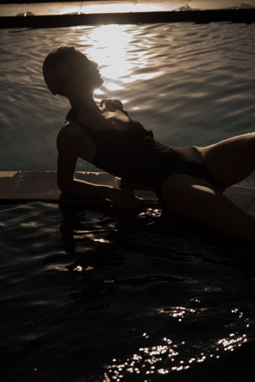 Free Silhouetted woman in swimsuit relaxing by a pool at sunset, capturing a serene tropical vibe. Stock Photo