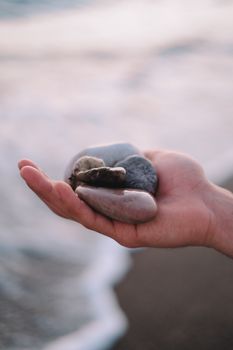 A hand gently cradling pebbles against a blurred ocean background.